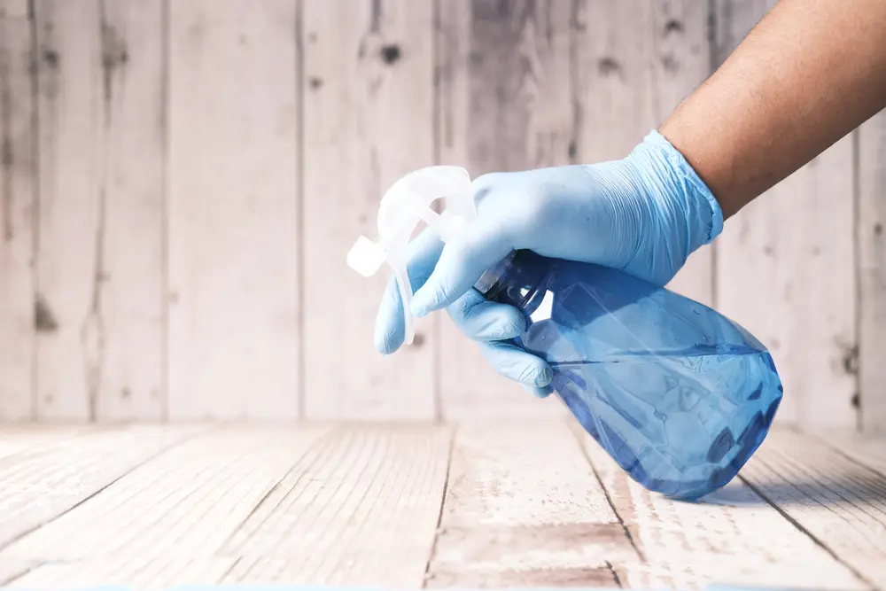 Gloved hand holding a spray bottle over a wooden surface